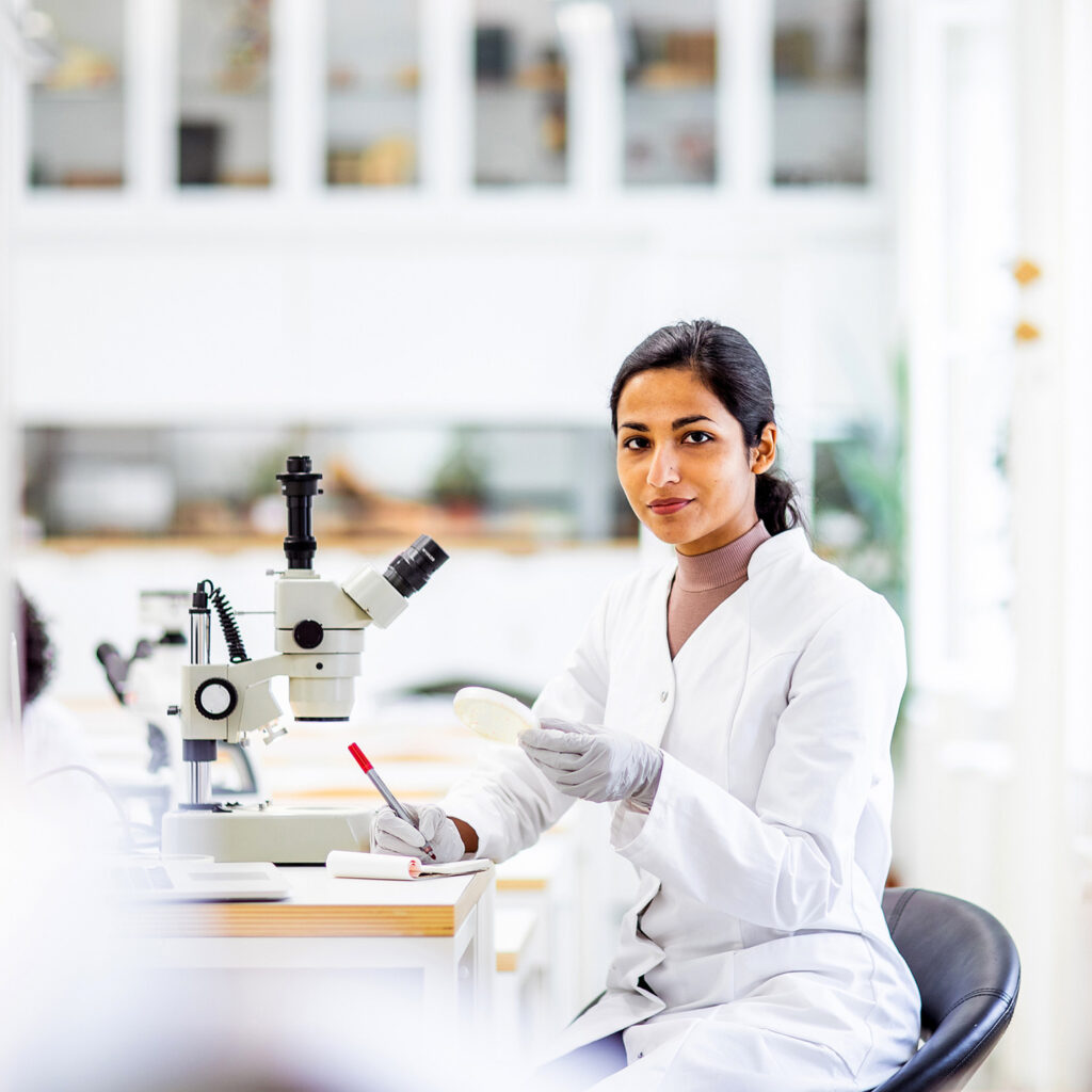 Wide shot van een onderzoeker die achter een microscoop zit.